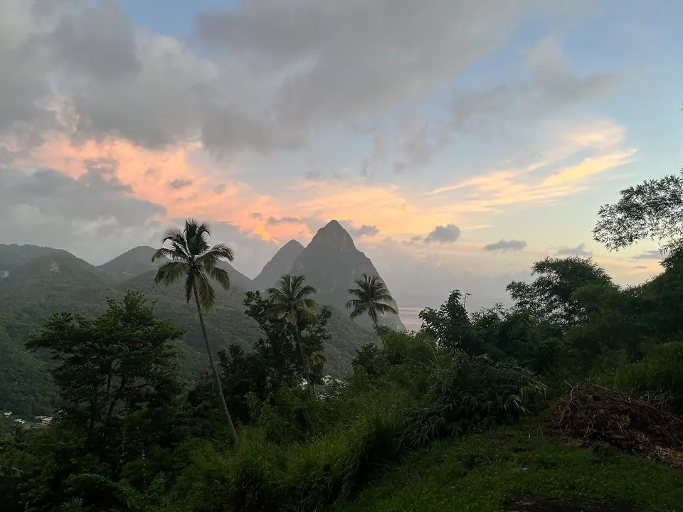 The twin volcanic Pitons of St. Lucia silhouetted against an orange sunset sky above palm trees