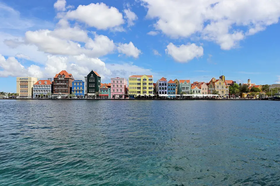 Row of colorful Dutch colonial buildings along the Handelskade waterfront in Willemstad, Curaçao, under a blue sky with white clouds