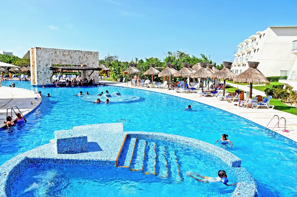 Large resort pool in Mexico with a swim-up bar, palapa umbrellas and sun loungers