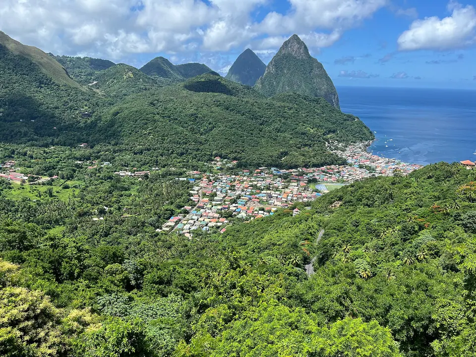 View across green hills to the town of Soufrière and the twin Pitons rising above the sea in Saint Lucia