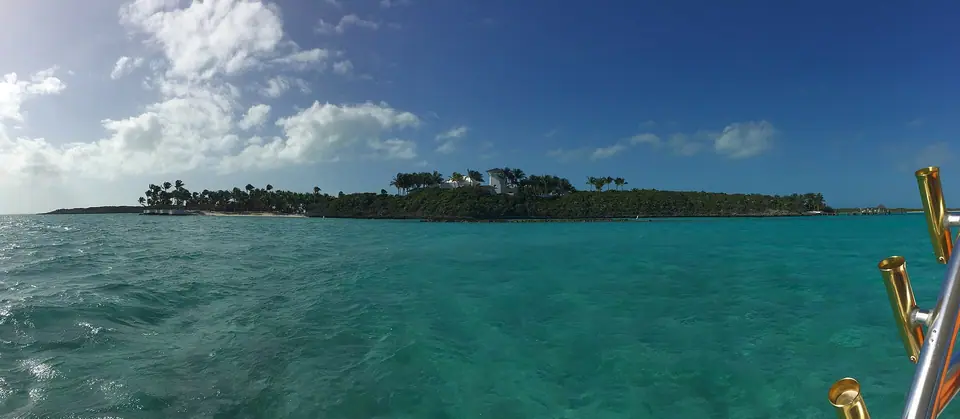 Low green cay fringed with palms and white sand rising from deep turquoise water in the Exumas, Bahamas